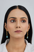 Woman wearing gold earrings with blue drops on a plain background