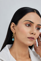 Woman wearing gold earrings with turquoise stones against a light gray background