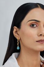 Woman wearing gold earrings with a blue gemstone